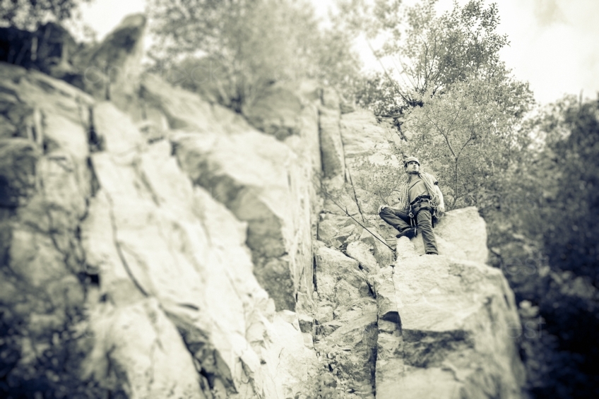  Mann mit Kletterausrüstung sitzt auf einem Berg s/w 20160718