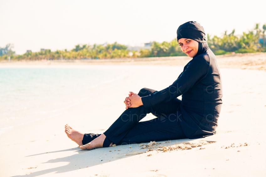 Frau im Burkini sitzt am Strand Seitansicht 20140313-3469