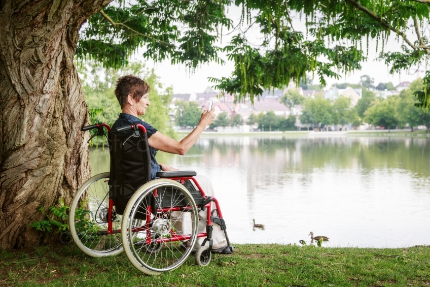 Frau in Rollstuhl macht Foto an See 20160725-0119