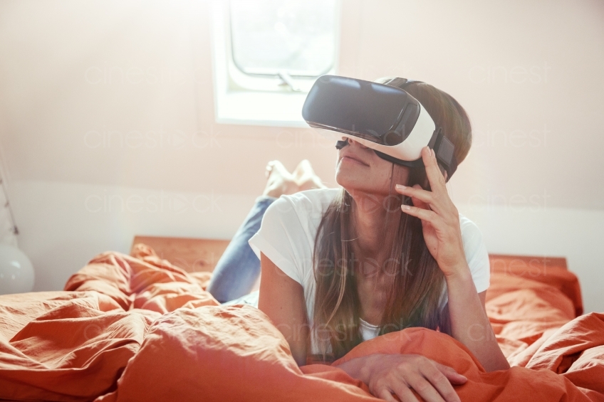 Frau liegt mit VR-Brille auf dem Bett 20160810