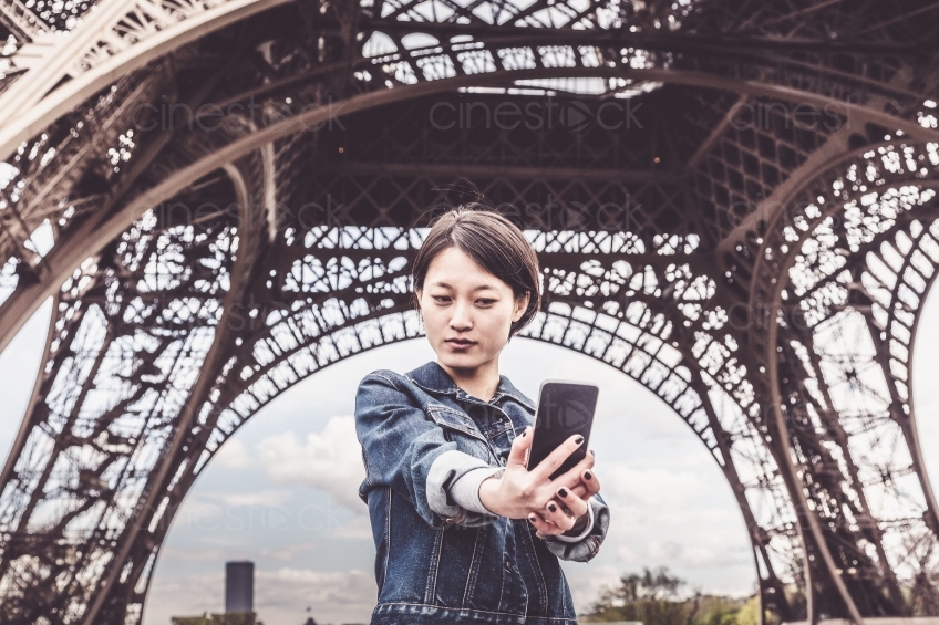 Frau macht Selfie vor dem Eiffelturm stehend 20160426