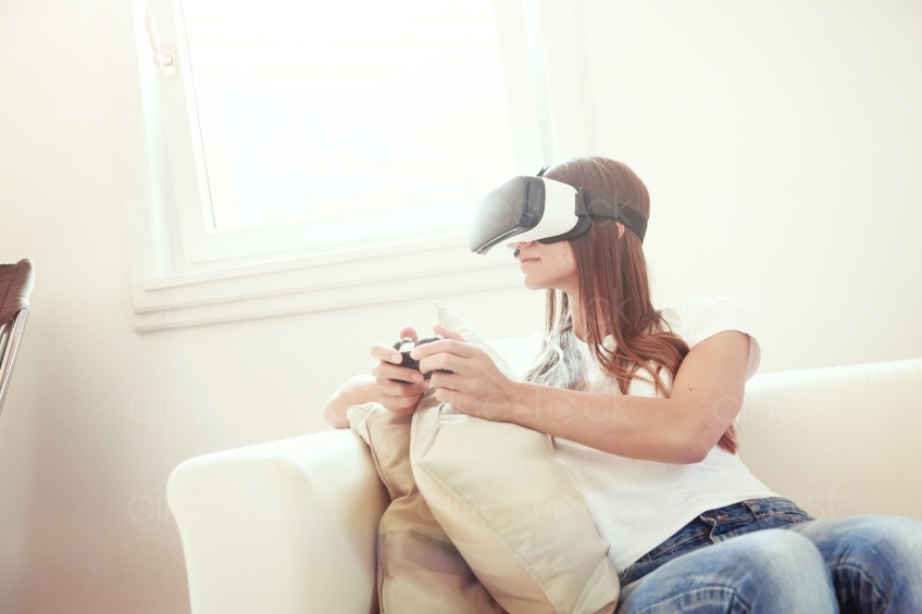 Frau mit VR-Brille und Joypad auf dem Sofa 20160810
