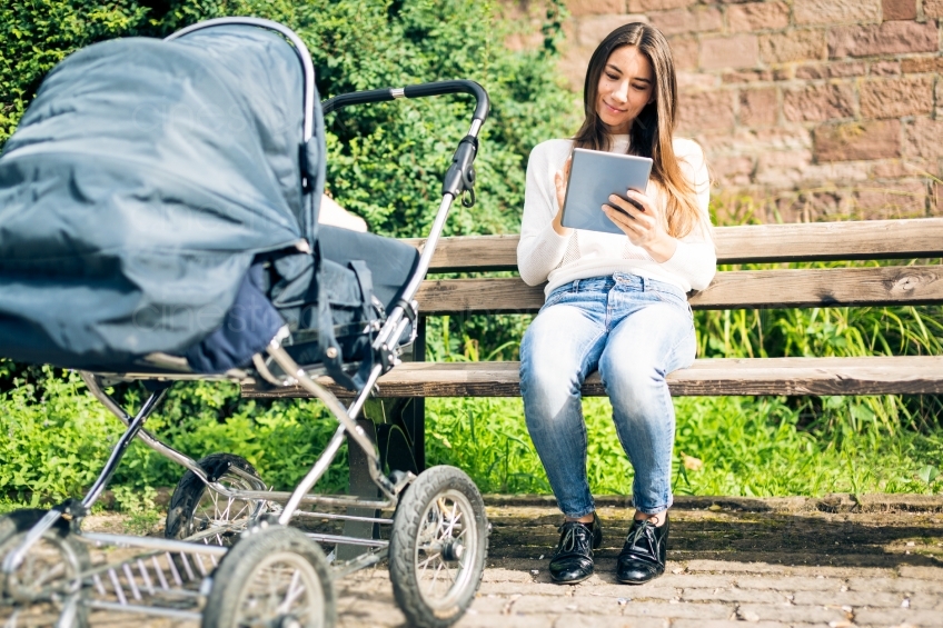Frau schaut auf Tablet mit Kinderwagen im Vordergrund 20160810-0048 