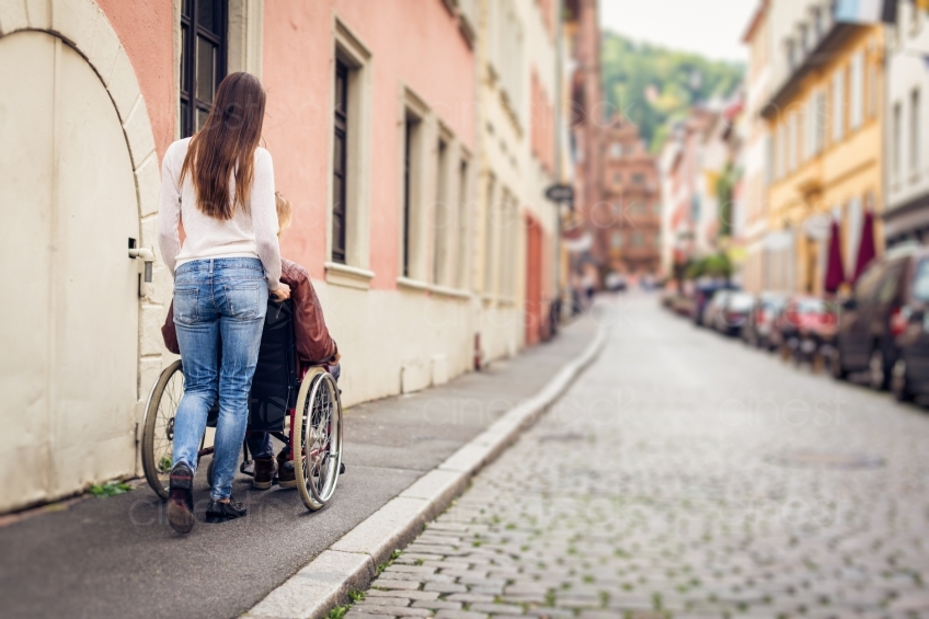 Frau schiebt Mann im Rollstuhl spazieren 20160810