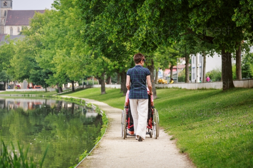 Frau schiebt Rollstuhl am See Rückenansicht 20160725-0552