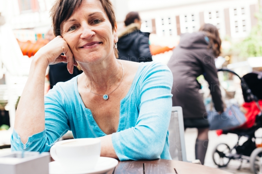 Frau sitzt mit Kaffee am Tisch 20160518