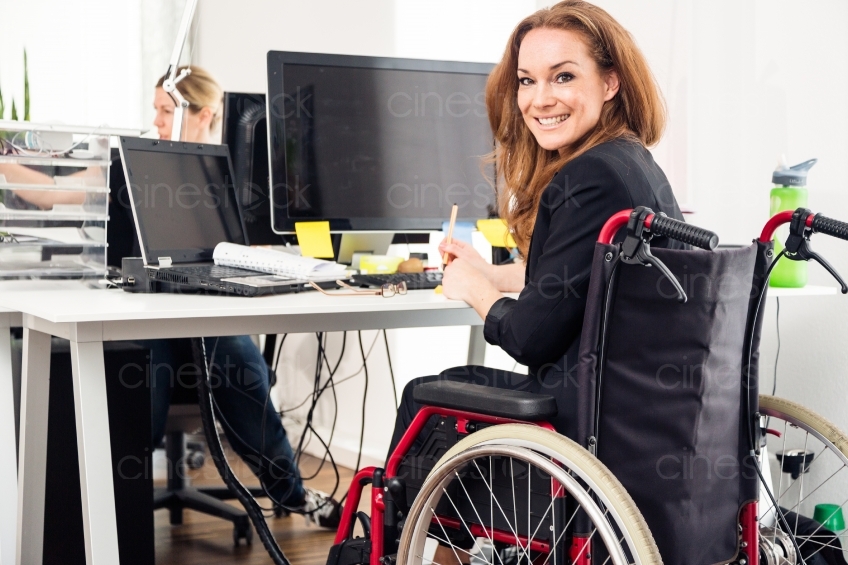 Lächelnde Rollstuhlfahrerin am Arbeitsplatz 20150510-0084