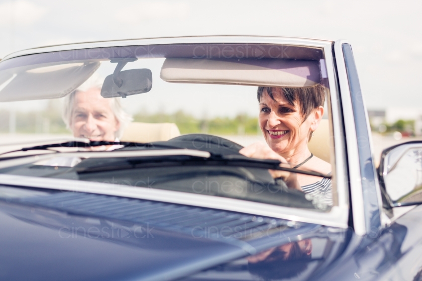 Älteres Paar lacht am Steuer von Cabrio 20150429-0363