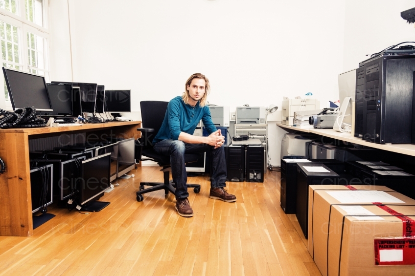 Mann auf Bürostuhl zwischen Computern 20150510-0578