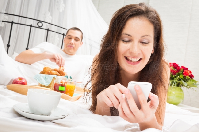 Mann Frühstückt im Bett und Frau ist am Handy 20121130