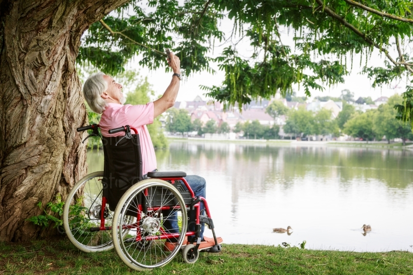 Mann in Rollstuhl macht Selfie an See unter Baum20160725-0108