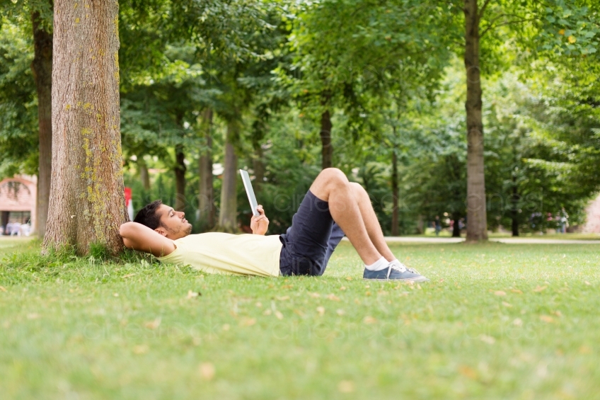 Mann liegt mit Tablet am Baum im Park 20130811-heidel-0832