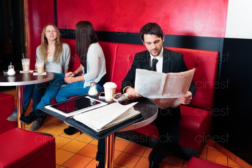 Mann mit Anzug und Zeitung und zwei Frauen im Café 20121117-121