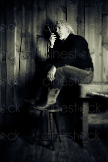 Mann mit Cowboystiefeln und Zigarre sitzt auf Tisch Graustufen 20160809-0049