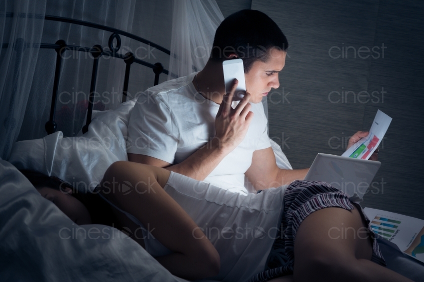 Mann mit Handy und Laptop im Bett 20121130-468