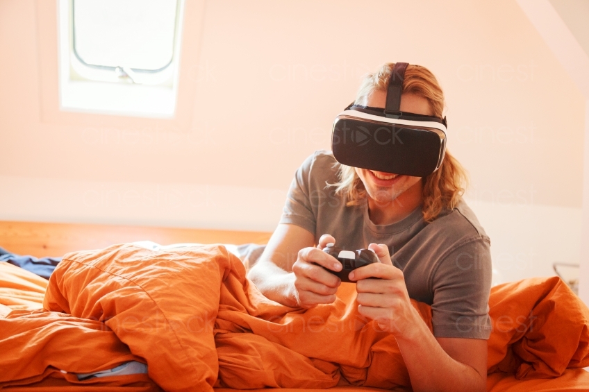 Mann mit VR-Brille und Joypad auf dem Bett 20160810