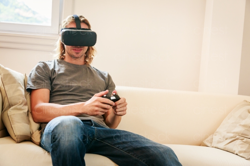 Mann mit VR-Brille und Joypad auf dem Sofa 20160810