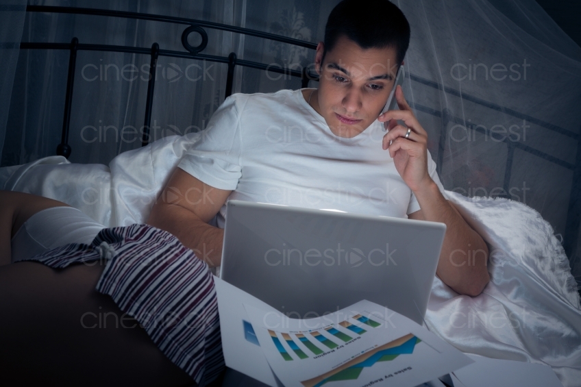 Mann sitzt mit Handy und Laptop im Bett 20121130-444 