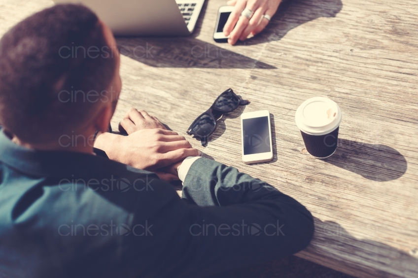 Mann sitzt mit Kaffee, Sonnenbrille und Handy am Tisch 20160426 