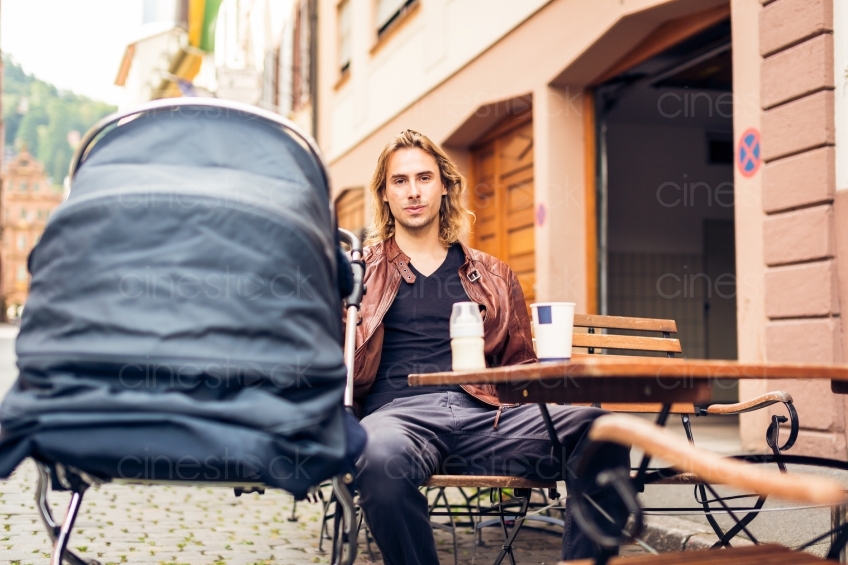 Mann sitzt mit Kinderwagen vor einem Cafe 20160810