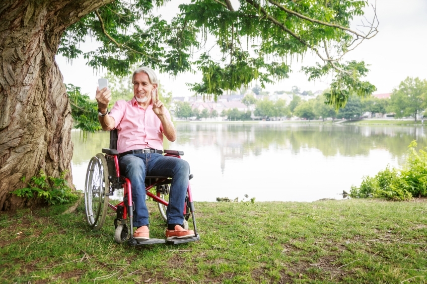 Rollstuhlfahrer macht Selfie am See mit Handzeichen 20160725-0160