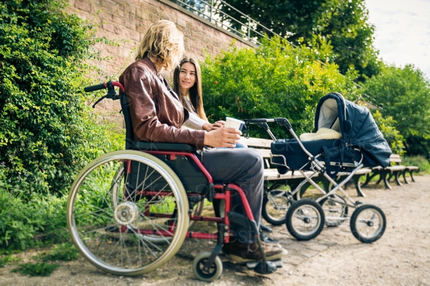 Rollstuhlfahrer mit Frau und Kinderwagen an Parkbank 20160810-0150