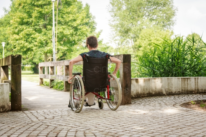 Rollstuhlfahrerin in Park an Brücke in Rückenansicht 20160725-0281