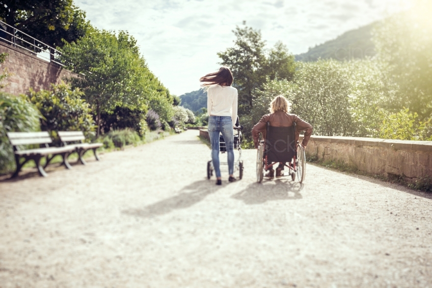 Rückenansicht von Frau mit Kinderwagen und Rollstuhlfahrer bei Spaziergang 20160810-0174